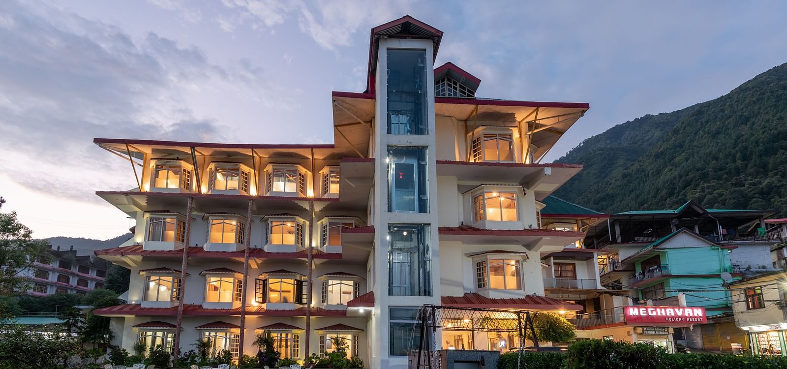 A well-lit hotel with a contemporary design, nestled amidst lush greenery and stunning mountain views - DLS Meghavan Resort